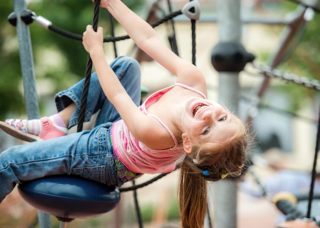 Funny smiling little girl playing at the playground and climb the ropes outdoor