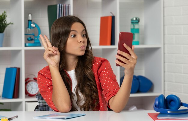 Funny teen girl making video on selfie using mobile phone showing peace gesture blogging