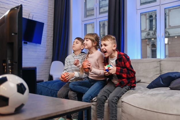 Funny three child friends are sitting on the couch at home and enjoying soccer match