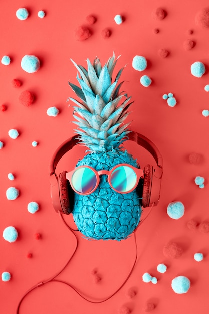 Funny turquoise pineapple in sunglasses and earphones on decorated red paper