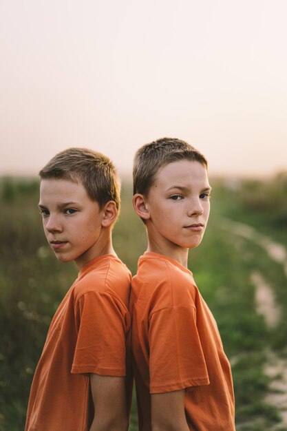 Funny twin brother boys in orange tshirt playing outdoors on field at sunset Happy children lifestyle