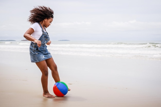 Funny vacation African American kid girl playing ball and having fun on a tropical beach