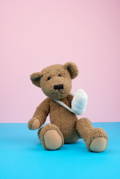 Funny vintage brown curly teddy bear with rewound paw with white gauze bandage