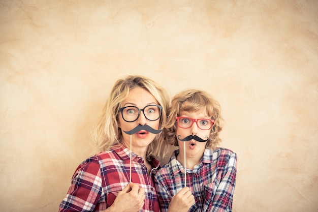 Photo funny woman and kid with fake mustache. happy family playing in home