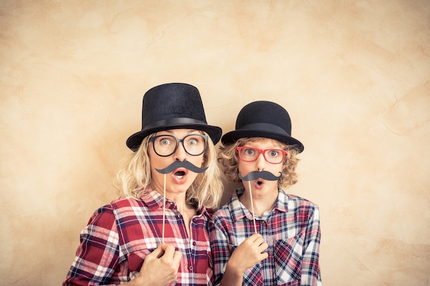 Funny woman and kid with fake mustache. Happy family playing in home