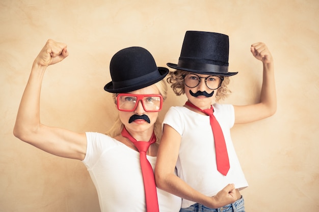 Funny woman and kid with fake mustache. Happy family playing in home