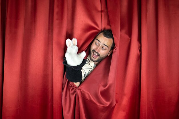 Photo funny young adult man magician with happy face playing with rabbit out hat