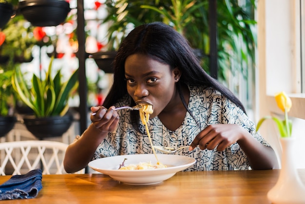 Funny young african woman eating tasty pasta in cafe