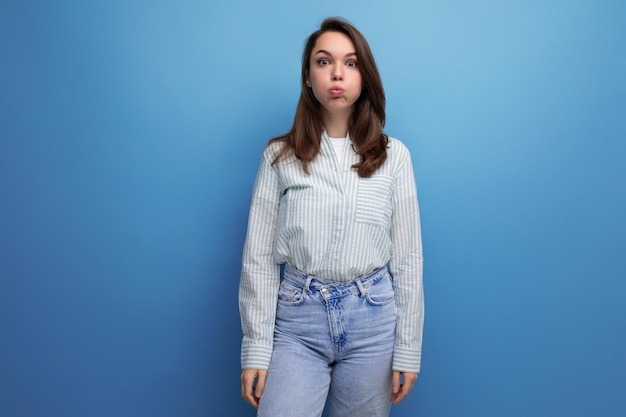 Funny young brunette lady dressed in a striped shirt and jeans grimaces and makes a face