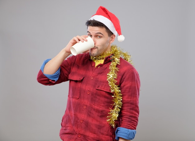 Funny young drunk man wearing Santa hat holding a paper cup