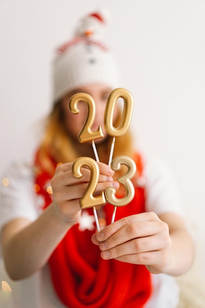 Funny young girl in a New Year's hat and red scarf holds the numbers 2023 in her hands New year and Christmas concept