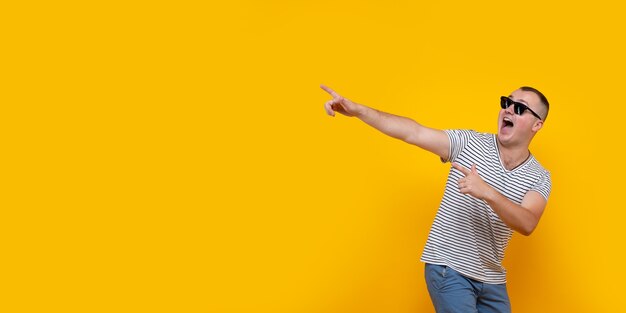 funny young man in casual clothes pointing fingers aside isolated on yellow background