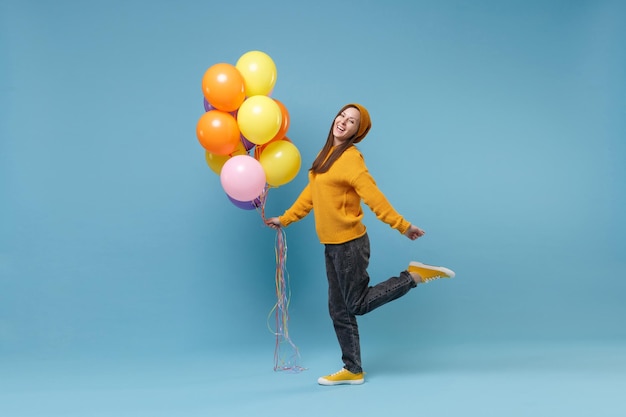 Funny young woman girl in sweater hat posing isolated on blue background studio portrait. Birthday holiday party people emotions concept. Mock up copy space. Celebrating holding colorful air balloons.