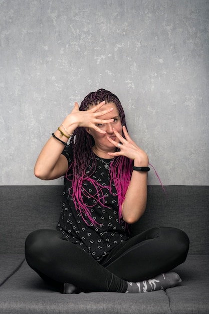 Funny young woman with dreadlocks sits on the couch and actively gesticulates Freaky girl Vertical frame