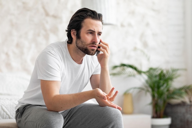 Furious guy having phone call sitting on bed