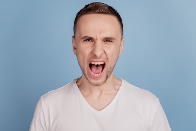 Furious man with grumpy grimace on his face mouth opened in shout conflict mad crazy isolated over blue background