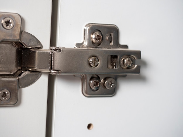 Photo furniture hinges for white wooden furniture door close-up.