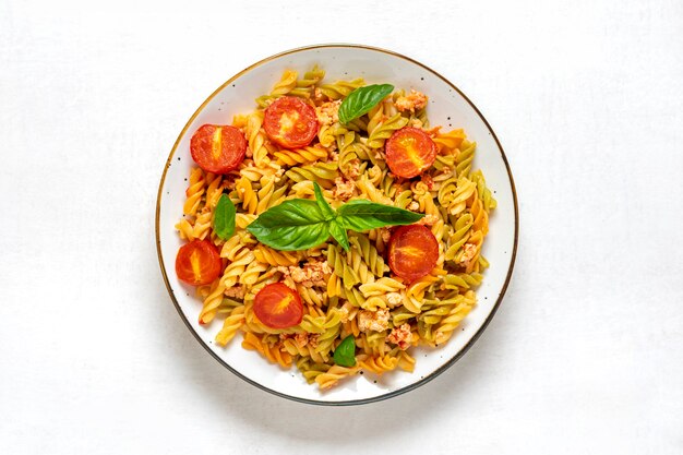 Fusilli - classic italian pasta from durum wheat with chicken meat, tomatoes cherry, basil in tomato sauce in white bowl on white wooden table Mediterranean cuisine Top view Flat lay.