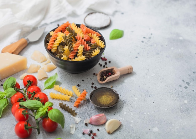 Fusilli pasta in black bowl with parmesan cheese and tomatoes oil and garlic with basil and linen towel on light background Space for text