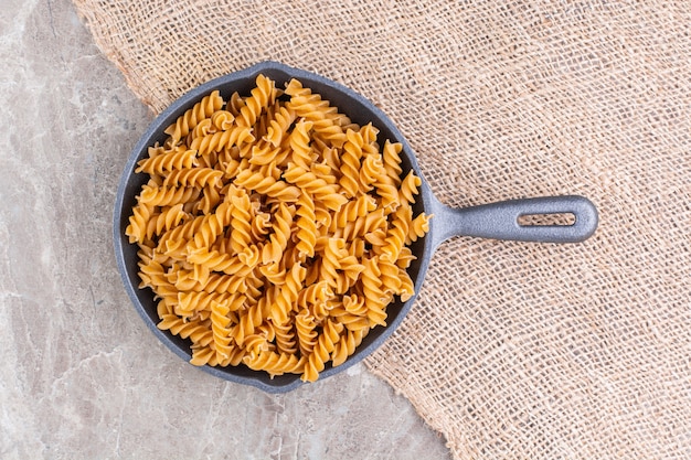 Fusilli pasta in a pan on a burlap, on the marble surface