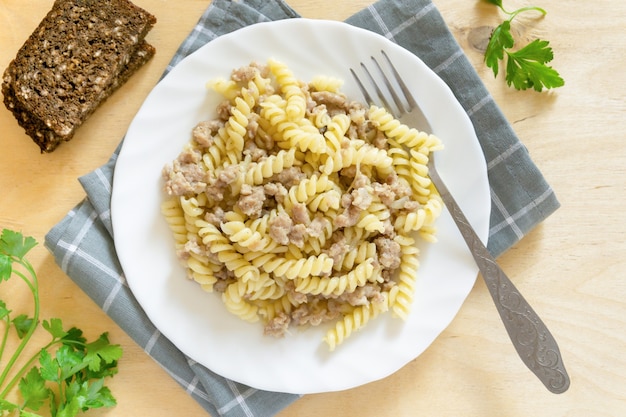 Fusilli pasta with minced meat on white plate, top view.