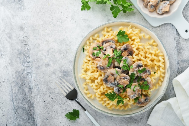 Fusilli pasta with mushrooms cheese and garlic creamy sauce on plate on on grey stone or concrete table background Top view Traditional Italian cuisine