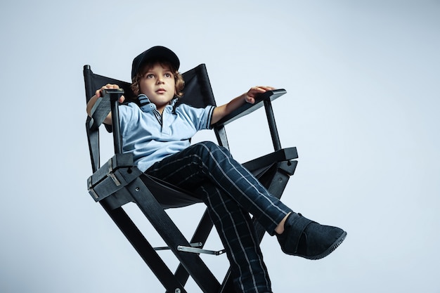 Future boss. Pretty young curly boy in casual clothes on white  wall. Confident and cool. Caucasian male preschooler with bright facial emotions. Childhood, expression, having fun.