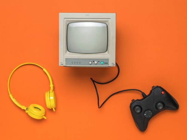 A game console, headphones and a gray monitor on an orange background.