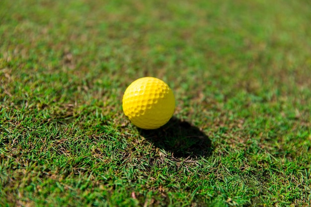 game, entertainment, sport and leisure concept - close up of yellow golf ball on green field grass