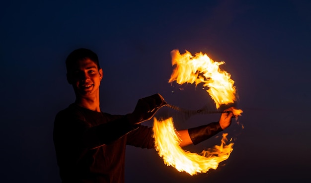 Game of light and dark Fire spinner at night Happy male spinner spin burning poi Fire performance Poi spinning and flow art Evening party Outdoor festival Celebrating holidays