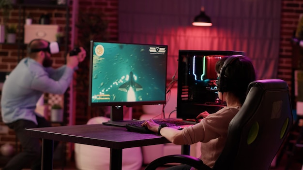 Gamer girl shocked after losing fast paced space shooter while boyfriend is enjoying virtual reality role playing game at home. Couple in online gaming competition using pc and vr goggles.