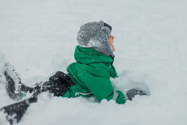 Games in winter in the fresh airA little boy in a green jumpsuit plays in the snow and sculpts a snowman