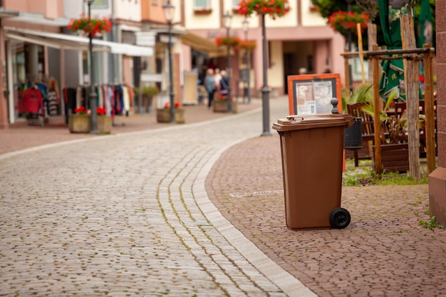 A garbage container stands on the street of a European German city. The street is paved with paving stones.