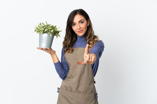 Gardener girl holding a plant isolated on white background showing and lifting a finger