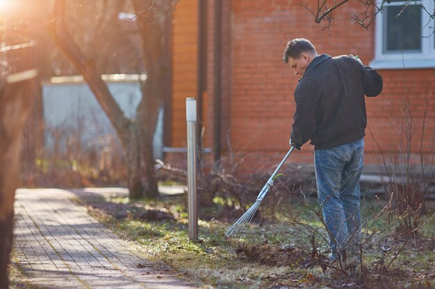 Photo gardener raking fall leaves in garden. copy space.