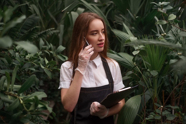 Gardener with mobile phone work in greenhouse.