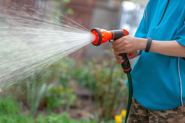 Gardener with watering hose and sprayer water on the flowers. Sparkling water spraying out of sprinkler on the green lawn. Summer gardening.