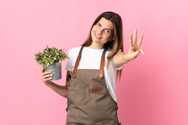 Gardener woman holding a plant isolated on pink happy and counting three with fingers