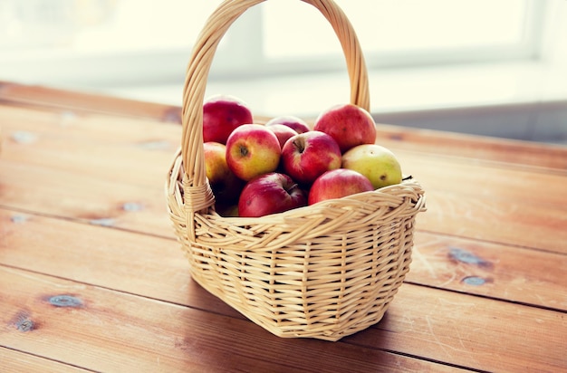 gardening, season, autumn and fruits concept - close up of wicker basket with ripe red apples on wooden table