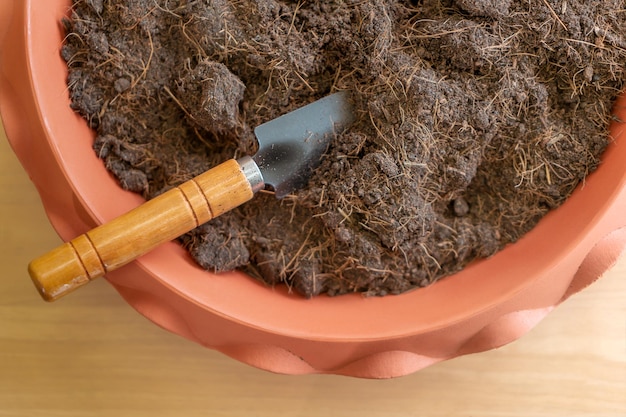 Gardening tools shovel is inside a soil in orange flower pot top view