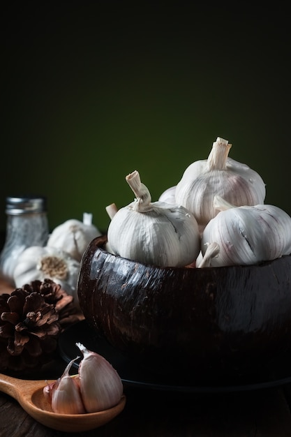 Garlic cloves and garlic bulb in half of coconut shell bowl on wooden table. 