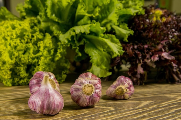 Garlic cloves and garlic bulb on a wooden board Green salad in the background Seasoning for the kitchen