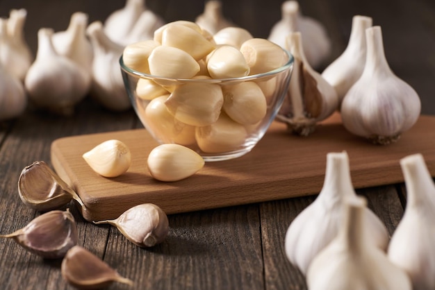 Garlic cloves in a glass bowl with peeled garlic on a wooden table.