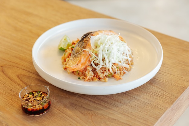 Garlic fried rice with grilled salmon served with chili bean sauce on wooden table.