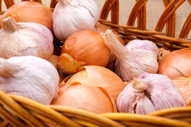 Garlic and onion bulbs are stacked in a wicker basket.