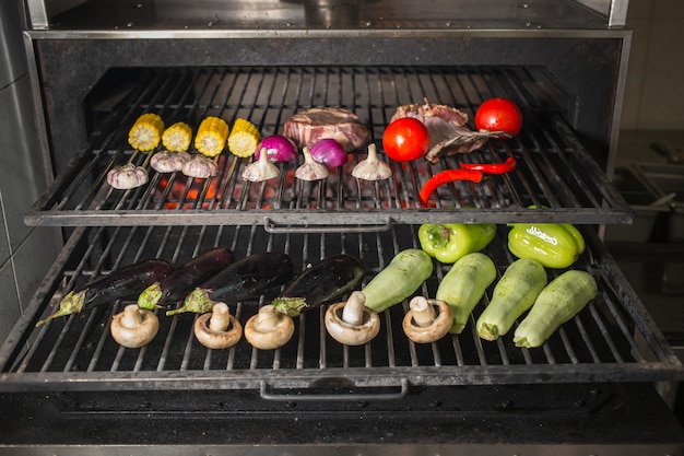 Garlic, onion, eggplant, zucchini, mushrooms, corn, pepper, tomatoes and meat on the grill on hot coals with smoke.