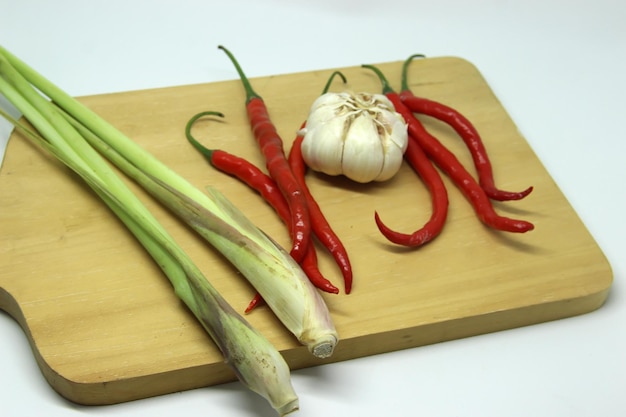 a garlic with a bunch of red chili peppers and lemongrass on wood cutting board