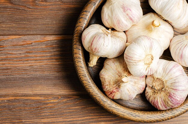 Garlic in a wooden plate Brown wooden background Copy space