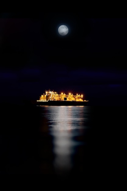 Photo gas carrier at night against the background of dark sea. tanker in the moonlight and bright lanterns on a ship with reflection in the water.