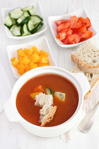 Gaspacho with bread and vegetables in white bowl